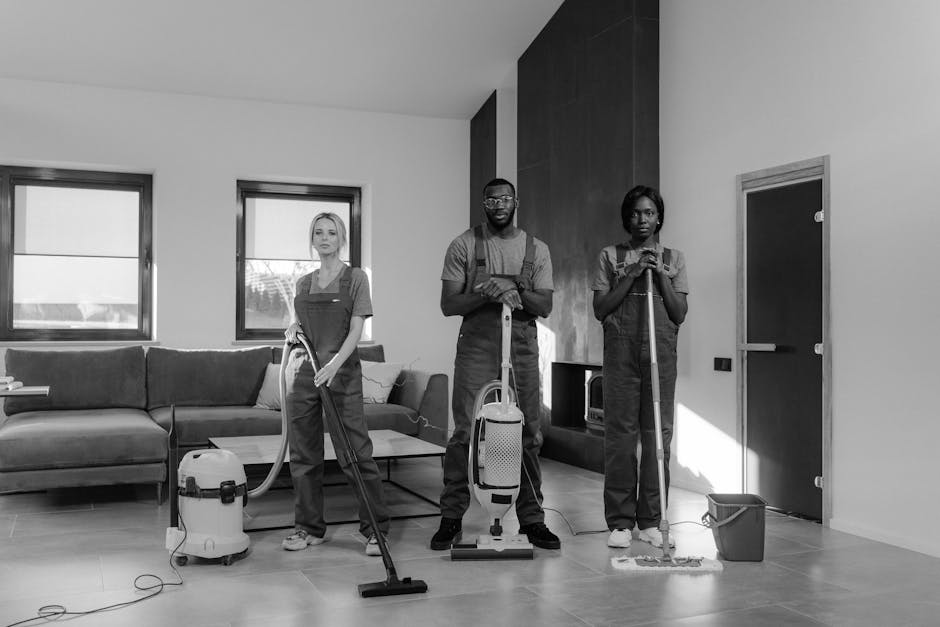Three professional cleaners from error code: 504 are performing surface cleaning and deep cleaning tasks in a modern living room with a minimalist design. The room features a large, L-shaped fabric so